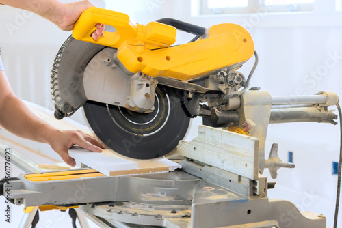 Photography Craftsman operates miter saw to cut wooden materials for project in well lit workshop setting