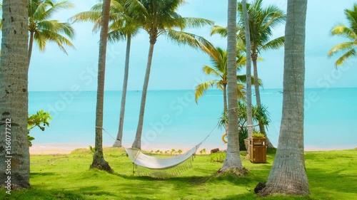 Hammock hanging between palm trees on tropical beach with turquoise sea and green grass with nobody, paradise setting for relaxation, summer vacation and peaceful escape, Phu Quoc island, Vietnam