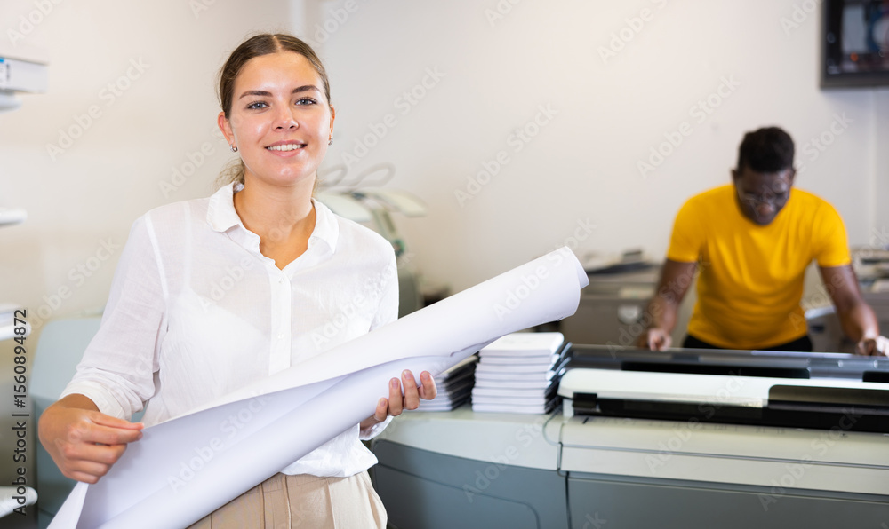 Obraz premium Portrait of friendly female employee of printing house with a stack of notebooks in her hands