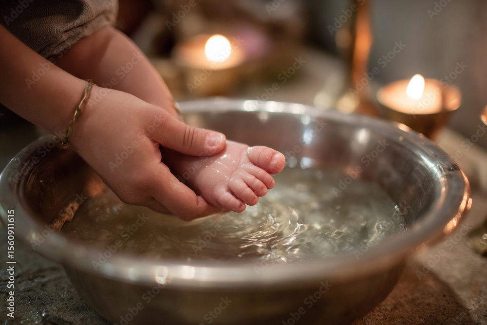 Fototapeta premium Close-up of baby’s tiny foot being dipped into silver baptismal font, soft candlelight reflection on water.