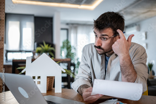 Fototapeta Confused man reading documents and calculating expenses for his new property