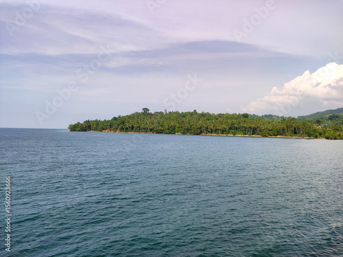 Tropical island coastline surrounded by calm blue sea, captured under a soft cloudy sky.