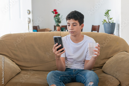 A boy is sitting on a couch and looking at his cell phone