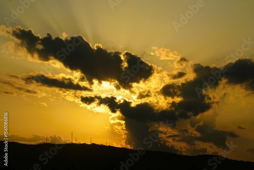 Golden sun paints the evening sky over a beautiful mountain landscape, silhouetted by the vibrant hues of a summer sunset or sunrise