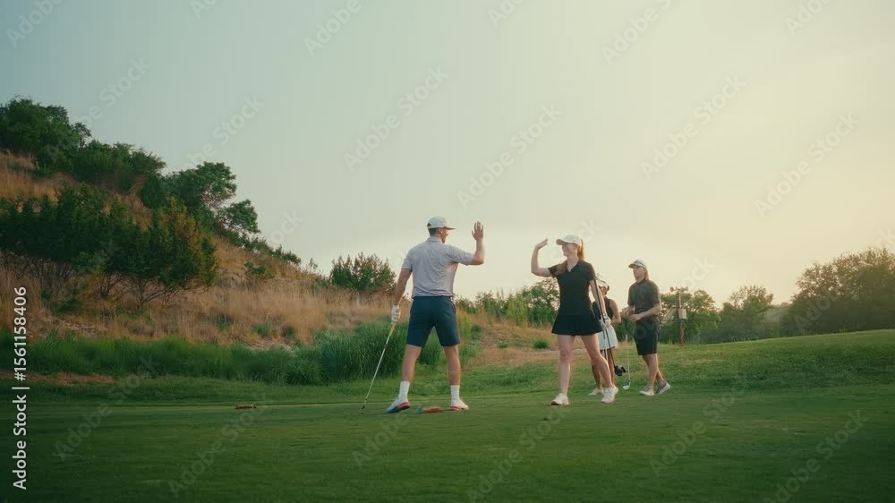 Golf foursome celebrates with a high five on the par 3 tee box after a male golfer hits a clean iron shot. Warm golden hour light highlights the group’s excitement and camaraderie on the course. Golf foursome celebrates with a high five on the par 3 tee box after a male golfer hits a clean iron shot. Warm golden hour light highlights the group’s excitement and camaraderie on the course.
