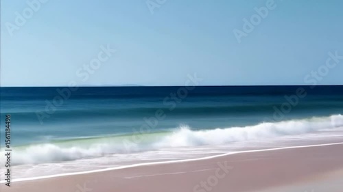 Coastal scene featuring the ocean and sandy beach a wave is rolling on the shore under a clear sky