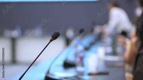 Microphone is on a table in front of a group of people. The microphone is black and red