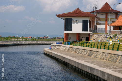 Modern Waterfront Building with Terracotta Roof Tiles Beside Calm Blue Canal on a Sunny Day