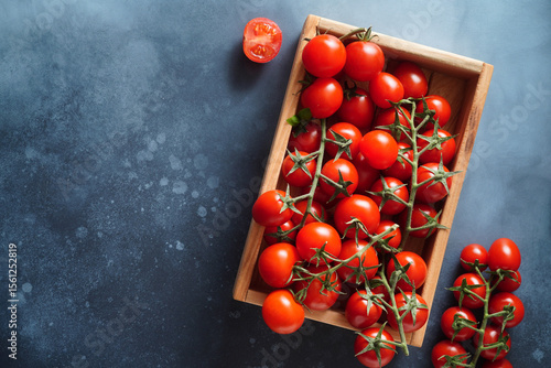 Tomatoes in wooden box on blue background. Fresh tomatoes on branch. Copy space. Top view.