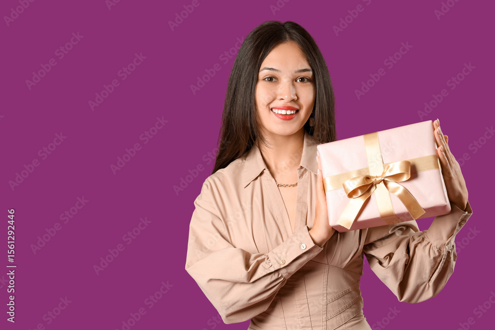 Beautiful young Asian woman with gift box on purple background Beautiful young Asian woman with gift box on purple background