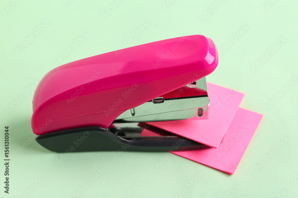 Pink stapler with sticky notes on green background Pink stapler with sticky notes on green background