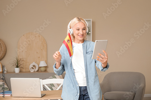 Mature woman in headphones with flag of Spain and tablet computer learning la...