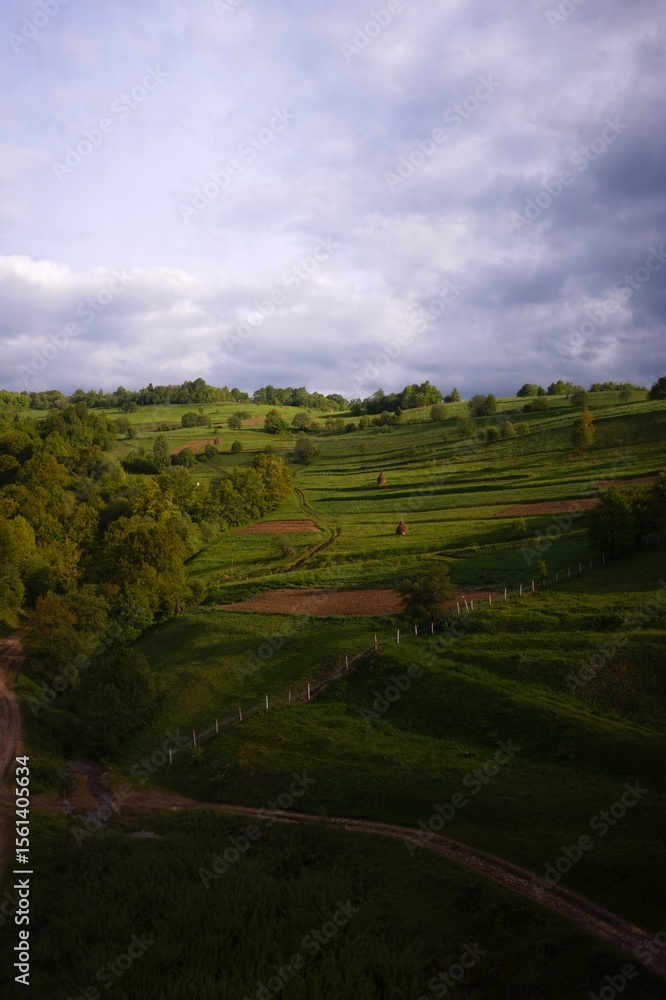 Obraz premium Idyllic countryside landscape with green rolling hills and dramatic sky.