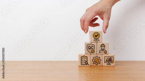 Business concept of quality assurance and control. Hand arranging wooden blocks with quality control, inspection, and performance icons in pyramid shape on wooden table in white background.