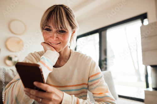 Woman with hand on chin using smart phone at home