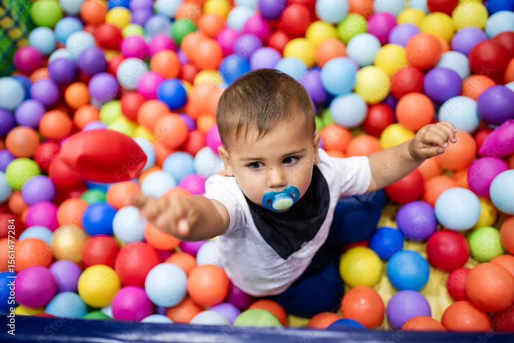 Baby boy playing with colorful balls in ball pit: throwing red ball and having fun Baby boy playing with colorful balls in ball pit: throwing red ball and having fun