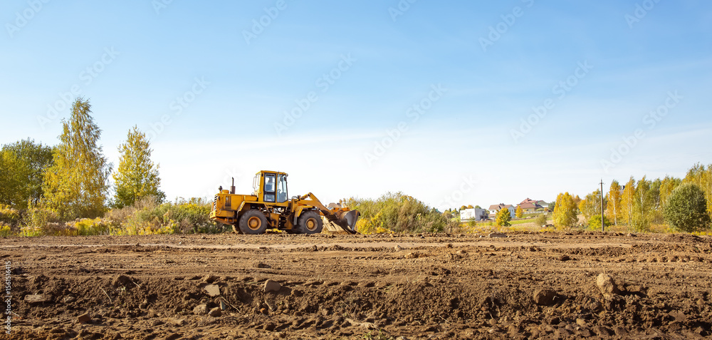 Fototapeta premium Yellow bulldozer at a construction site. Big wheel excavator leveling and clearing the land plot side view. Moving earthworks soil. Copy space. Building area. Special transport. High quality photo.
