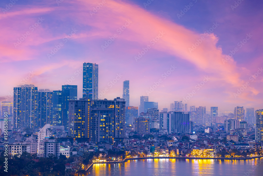 Fototapeta premium Hanoi skyline at sunset with pink clouds and illuminated buildings reflecting on water