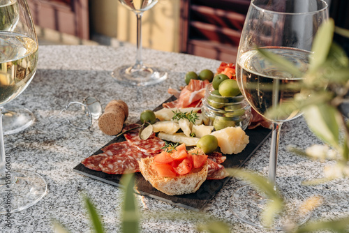 Food antipasto prosciutto ham, salami, olives and grissini bread sticks. cheese on a board parmesan, pecorino, gorgonzola. Charcuterie board. Two glasses of white wine or prosecco