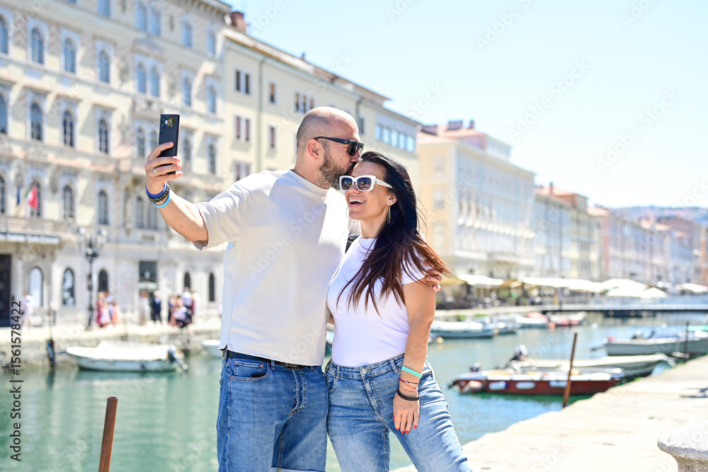 Fototapeta premium Trieste ,Italy, Canal Grande .Happy smiling couple of tourists making photos near Canal Grande at Trieste .Concept of Italian gastronomy and travel. Italian couple having fun together
