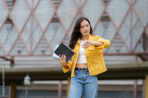 Fotografie Impatient student checking time while holding books in university campus