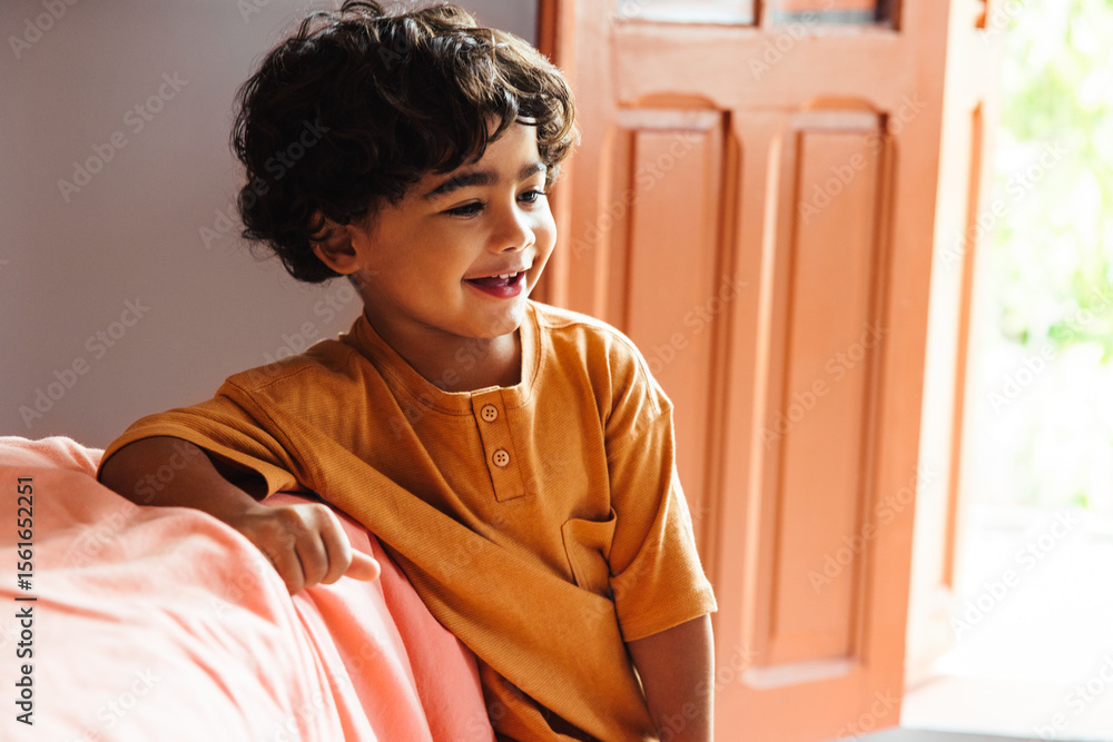 Fototapeta premium Cheerful young Latin American boy smiling indoors beside an open door