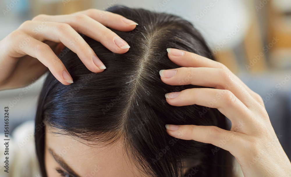 Naklejka premium Top view closeup portrait of a young woman examining her scalp and black hair looking at gray hairs at the roots standing at home. Brunette female person with graying head indoors.