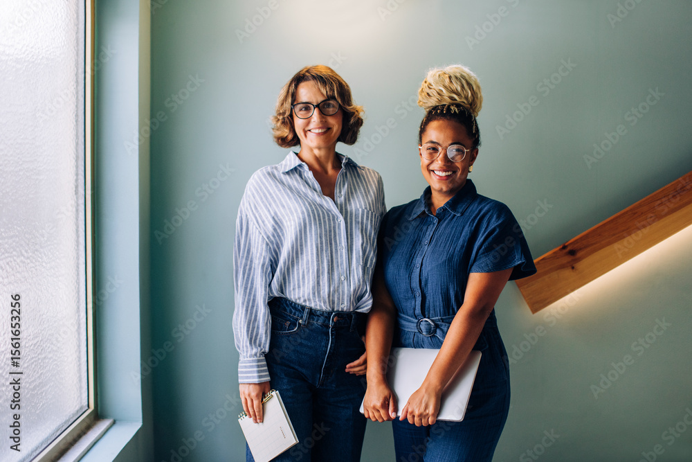 Fototapeta premium Two women standing together smiling in a casual office environment