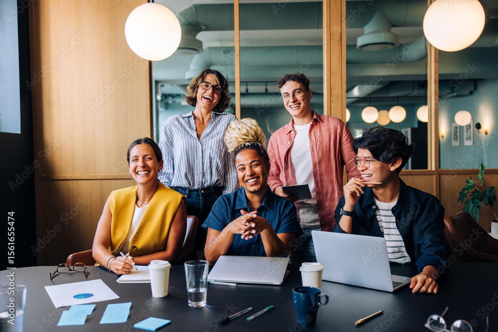 Obraz premium Group of young professionals laughing together at a meeting in an office