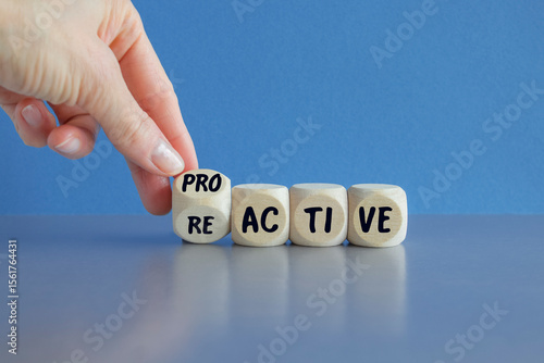 Businessman hand turns cubes and changes the word reactive to proactive. Beautiful blue background, grey table. Business and reactive or proactive concept