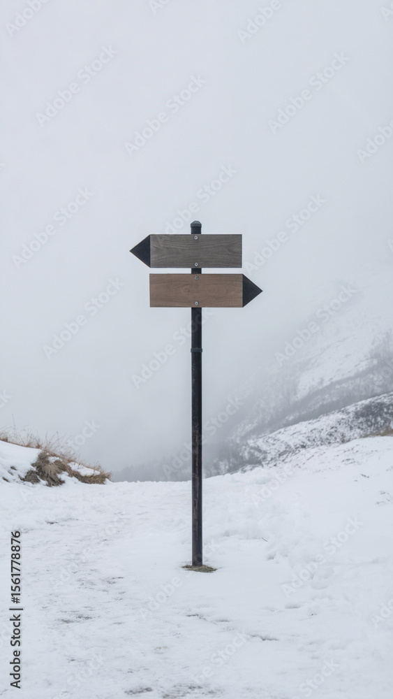 Naklejka premium A minimalist photograph of a black metal directional signpost in a snow-covered landscape