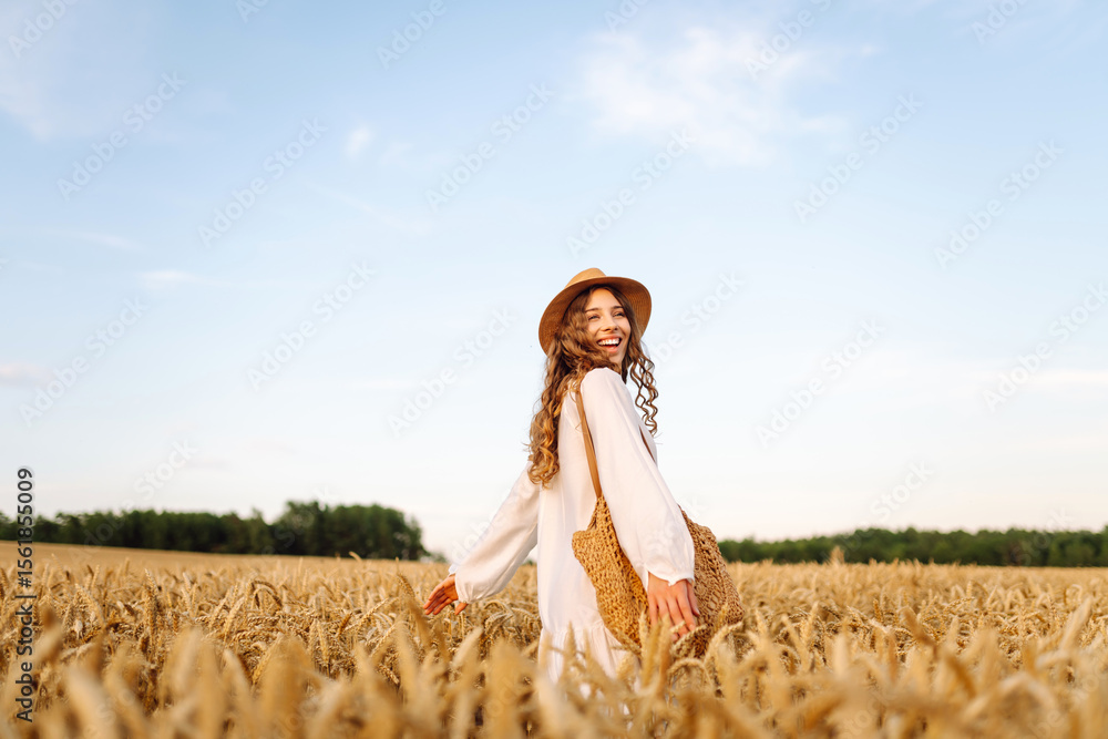 Obraz premium Joyful woman in white dress posing in golden wheat field. Young woman having fun and enjoying sunny weather outdoors. Nature and enjoyment concept.