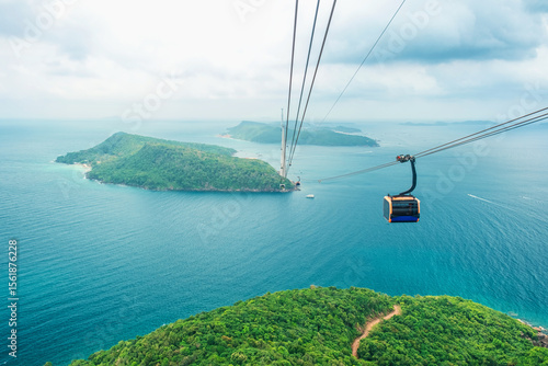 Fotografie Cable car cabin gliding over turquoise sea and green tropical island