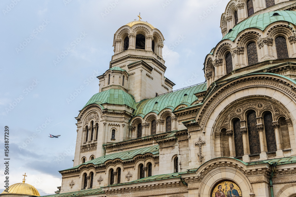 Fototapeta premium Close-Up Side View of Alexander Nevsky Cathedral in Sofia, Bulgaria with Airplane in Sky and Architectural Details of Dome and Arches