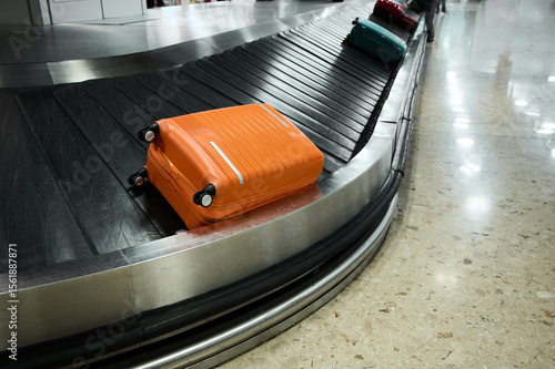 Bright orange suitcase and others waiting on the baggage carousel at a busy airport terminal during travel season
