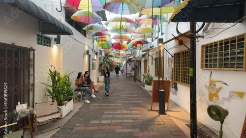 A charming alleyway on Armenian Street features vibrant umbrellas overhead, creating a picturesque scene while people are taking photos. George Town heritage site. tourist spot
