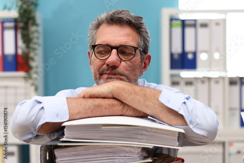 Office worker with glasses looks over a stack of files, looks unfocused and bored