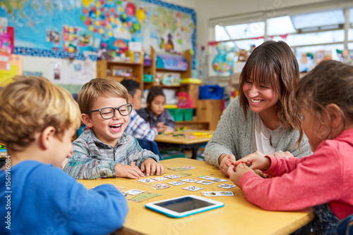 Group of children with special needs smiling and laughing while playing board games in classroom as teacher watches. Inclusive education, joy, and teamwork concept.

