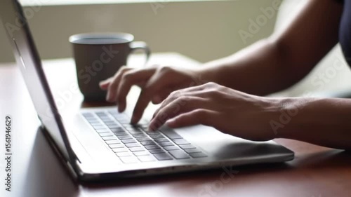 Close-up of a person’s hands typing on a laptop keyboard with a coffee mug in the background, suggesting remote work or freelance lifestyle.