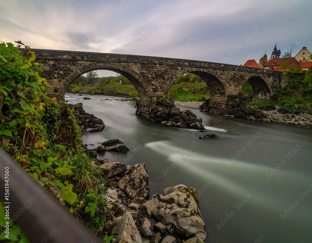 Fototapeta premium Ancient Stone Bridge Over a River in a Picturesque Landscape