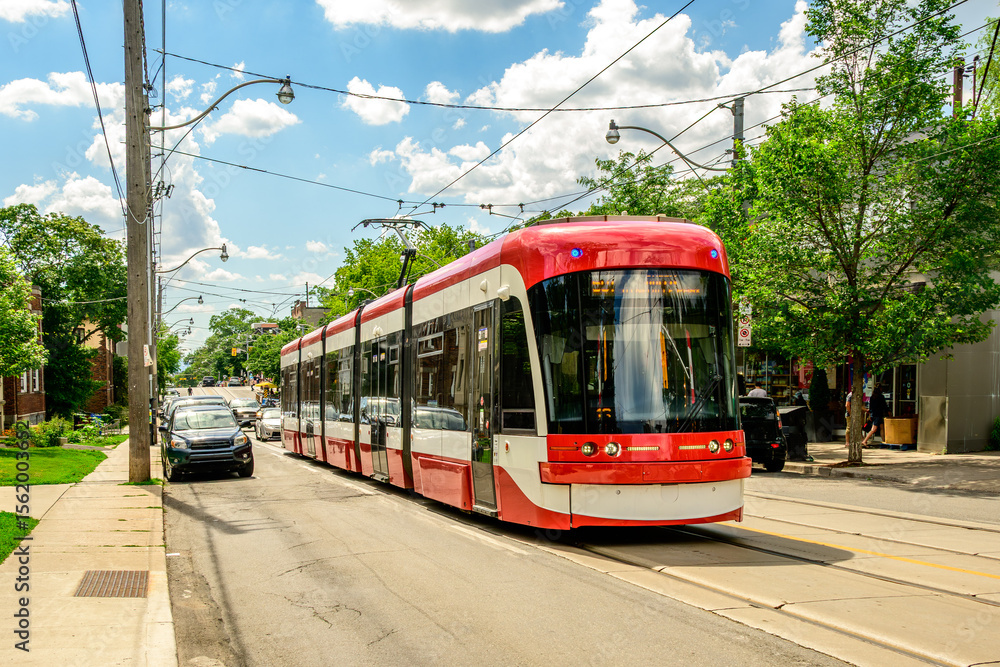 Naklejka premium Public transit: Streetcar on a summer day in the Toronto Beaches neighbourhood white clouds blue sky red tram 