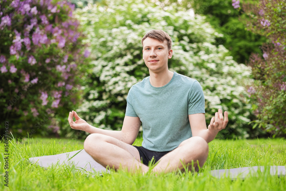 Obraz premium Young man practicing yoga on mat in park