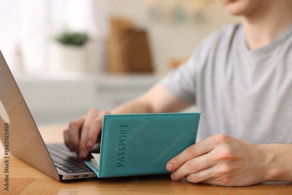 Fototapeta premium Man with passport using laptop at wooden table indoors, closeup