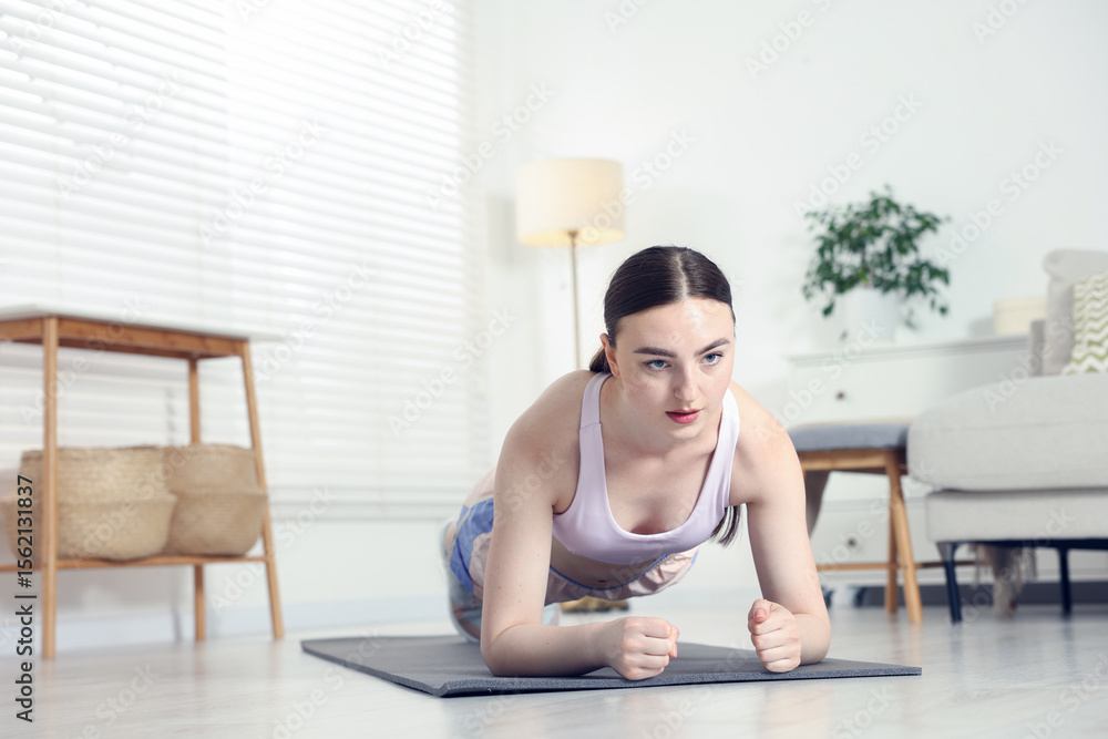 Fototapeta premium Young woman in sportswear doing plank exercise at home. Space for text
