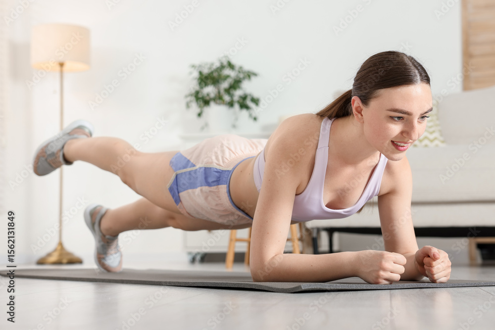 Obraz premium Smiling woman in sportswear doing plank exercise at home