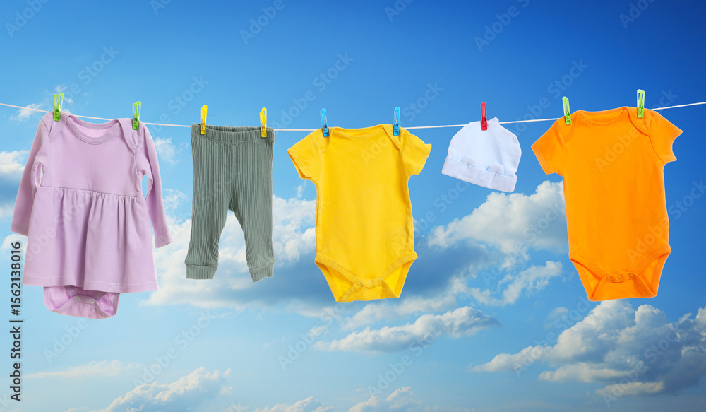 Different baby clothes drying on washing line against blue sky Different baby clothes drying on washing line against blue sky