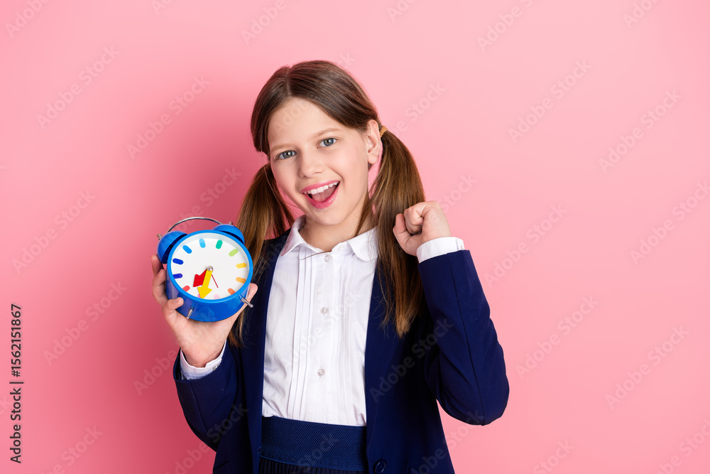 Excited schoolgirl holding blue clock in hands against pink background preparing for learning and school activities. Excited schoolgirl holding blue clock in hands against pink background preparing for learning and school activities.