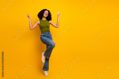 Attractive young woman in casual green top and jeans posing joyfully in front of vibrant yellow studio background