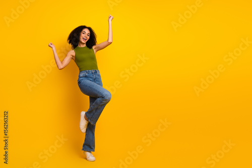 Fashionable young woman in casual attire smiling and posing energetically against a vibrant yellow background, expressing joy