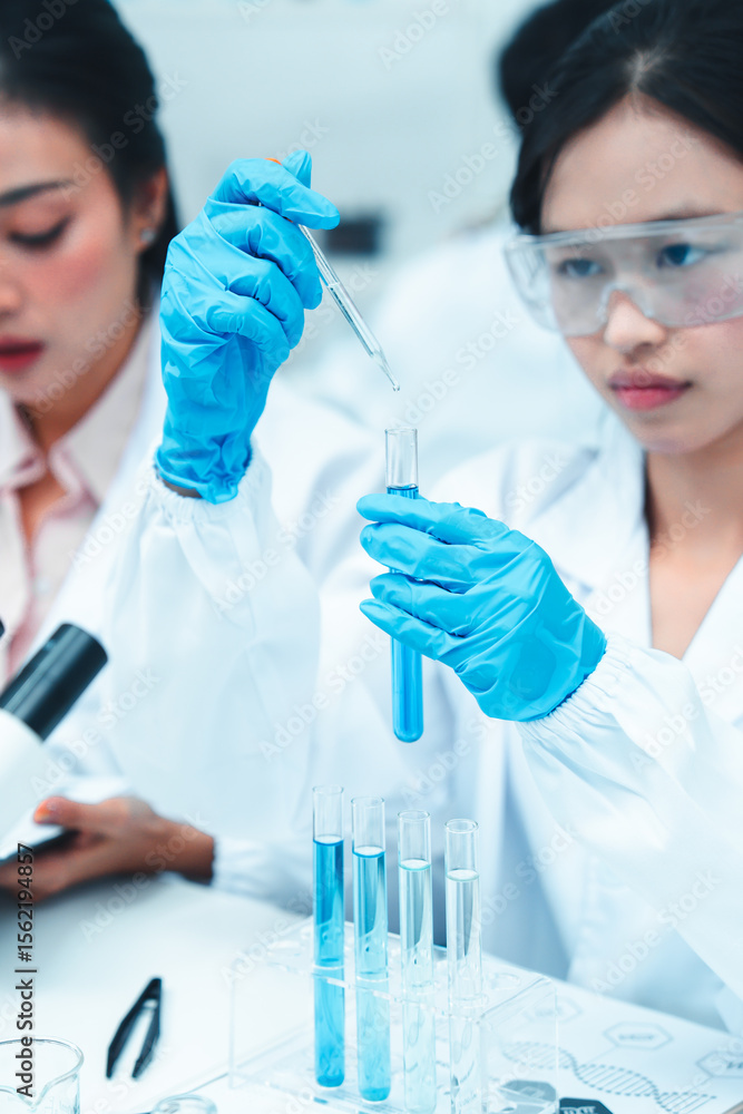 Two female scientists working in a modern laboratory. One is carefully transferring liquid with a pipette while the other observes and takes notes. STEM education and teamwork in a research setting. Two female scientists working in a modern laboratory. One is carefully transferring liquid with a pipette while the other observes and takes notes. STEM education and teamwork in a research setting.